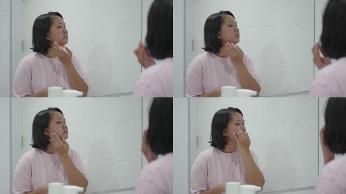亚洲女性在镜子里看自己的脸涂面霜