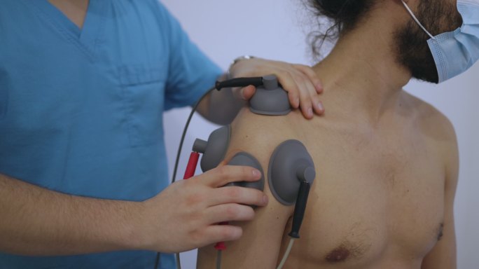 靠近一名男性患者的胸部，医生将电极调整到他的肩膀上