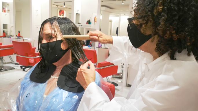 在沙龙重新开放时，女性蒙面美发师为顾客的头发定型