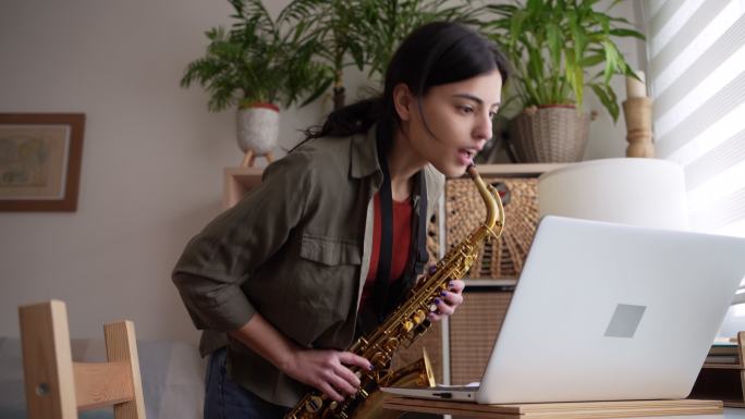 高加索女性，在笔记本电脑上观看在线教程，同时学习萨克斯管演奏