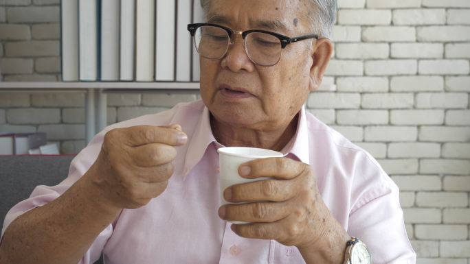 一位患有帕金森病的亚洲老人双手颤抖，试图服用这些药丸。