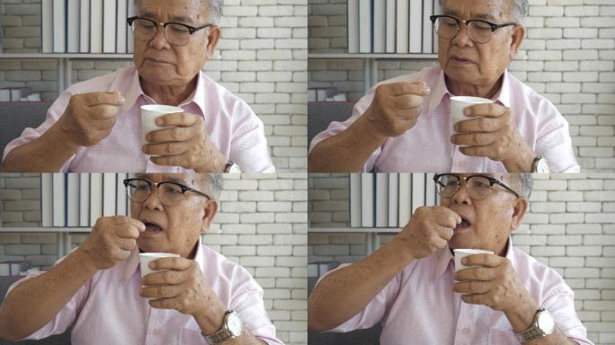 一位患有帕金森病的亚洲老人双手颤抖，试图服用这些药丸。