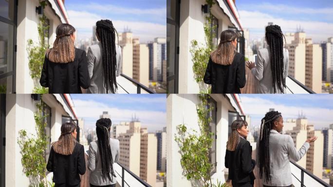 商业伙伴交谈/房地产经纪人向女性展示公寓阳台上的景色