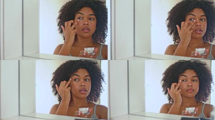 4k视频片段，一名女性一边看着浴室镜子一边涂眼霜