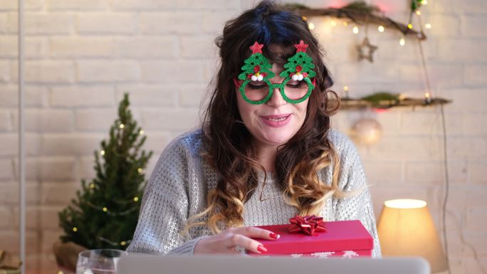 一位美女在家的特写镜头，在笔记本电脑上进行视频通话，打开圣诞礼物。