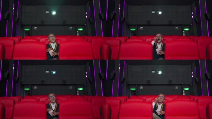广角正面图亚裔华人活跃老人独自在电影院看电影时，一边吃着点心