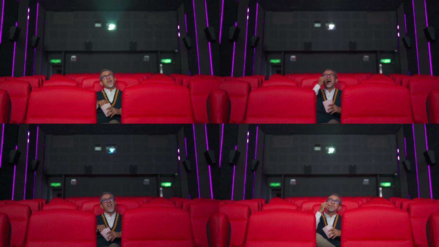 广角正面图亚裔华人活跃老人独自在电影院看电影时，一边吃着点心