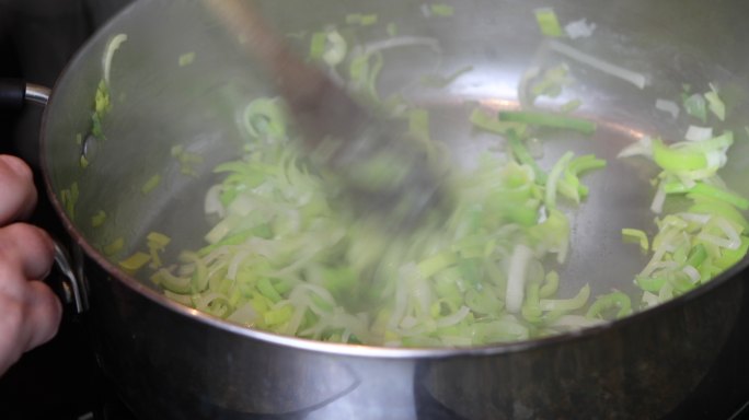 在大型不锈钢砂锅中炸碎韭菜，用木勺搅拌