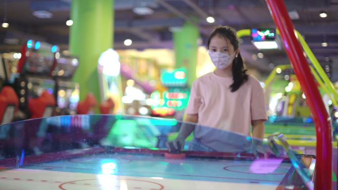 戴着口罩的亚洲女孩一起在游乐场玩空中曲棍球游戏，在新冠肺炎疫情锁定后重新开放