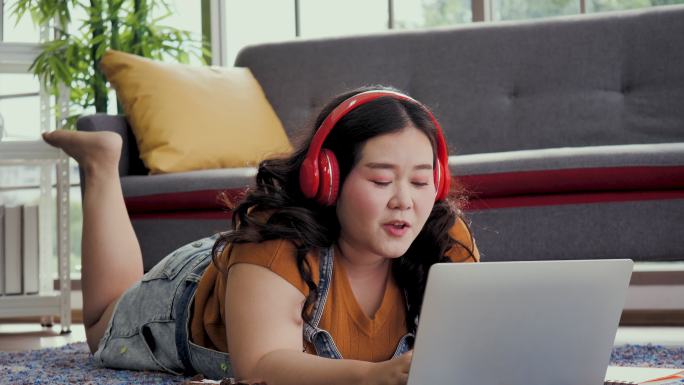 身材高大的女人在家里用笔记本电脑工作，亚洲女孩喜欢在家里的沙发上吃东西