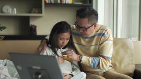 亚洲华人父亲在沙发上为生病的女儿量体温客厅通过数字平板电脑与医生视频通话视频素材