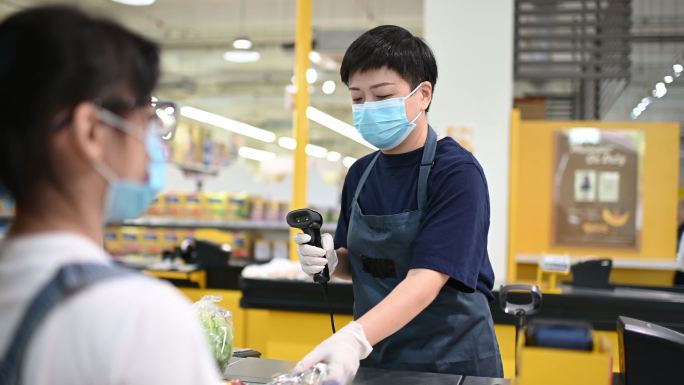 一位亚裔中国女性超市零售商售货员在柜台结账时扫描蔬菜的价格