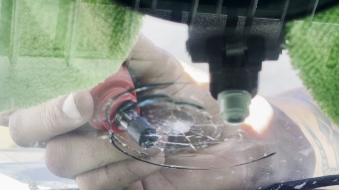 汽车玻璃修理工将聚合物注入汽车挡风玻璃上的一条大裂缝中，这条裂缝是开车时岩石造成的