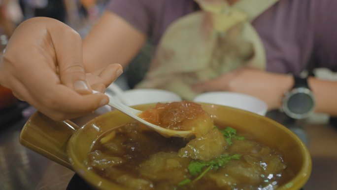 曼谷唐人街Yaorawat一家街头美食餐厅的金属桌上，用塑料汤匙盛着一碗热气腾腾的鱼肚汤。与美食携手
