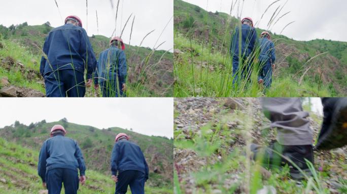 两名工人行走在长满杂草的山坡上