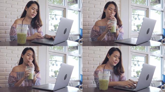 美丽的亚洲年轻女子在咖啡馆用笔记本电脑和喝牛奶绿茶