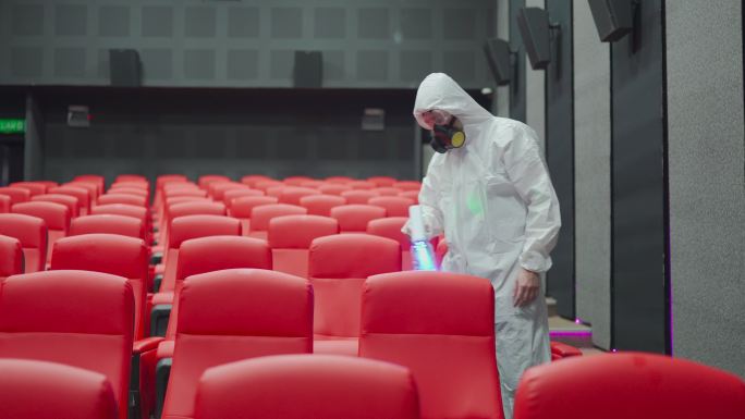 电影放映前，亚裔中国电影院清洁工戴着口罩和防护服在电影院大厅的椅子和地毯上进行消毒