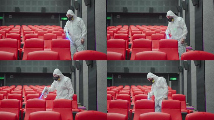 电影放映前，亚裔中国电影院清洁工戴着口罩和防护服在电影院大厅的椅子和地毯上进行消毒