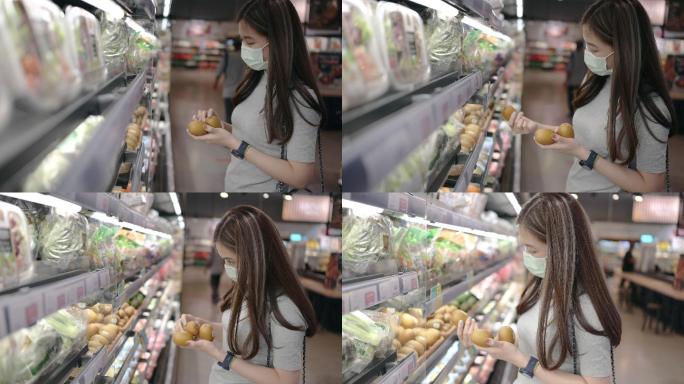 社交距离概念亚洲女性戴防护面罩，晚上在超市选择猕猴桃、蔬菜和水果