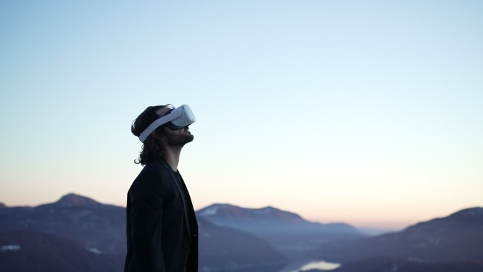 戴着VR虚拟现实护目镜的男子在山中的户外，在夕阳下俯瞰湖面，环顾四周