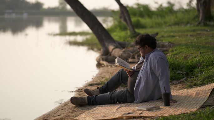 年轻人坐在河岸上看书。