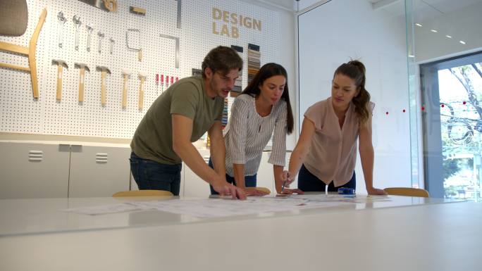快乐的室内设计师团队正在进行一个项目，一边聊天，一边微笑，一边看蓝图和色样