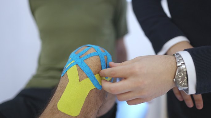 匿名物理治疗师在患者膝盖上使用运动录像带