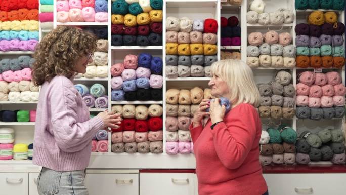 年轻女售货员帮助女性资深客户选择羊毛颜色