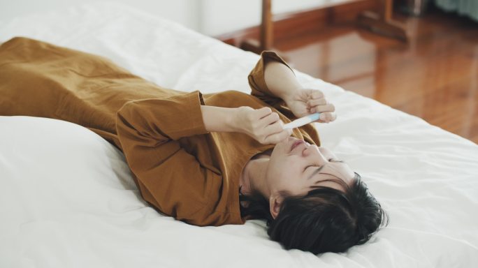 躺在床上拿着阳性妊娠检测试剂盒的亚洲女性