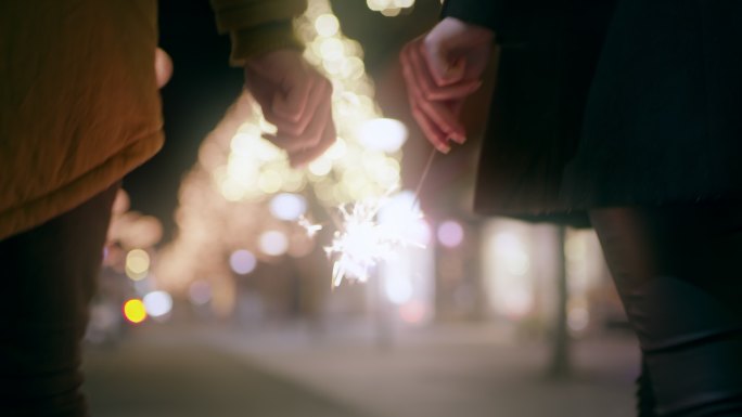 远景：圣诞节期间，一对夫妇在城里散步时手里拿着火花