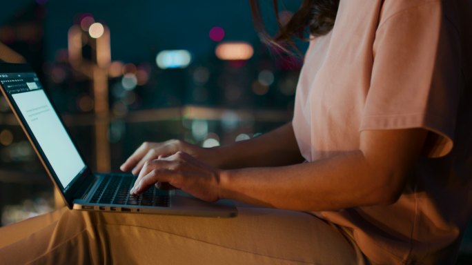 年轻女子的手在城市之夜使用笔记本电脑