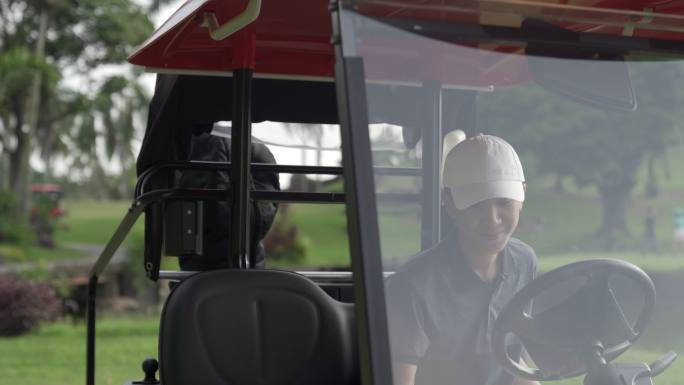 年轻的亚洲中国男子高尔夫球手在高尔夫球场驾驶高尔夫球车并打开装备