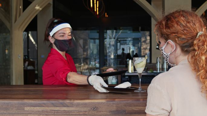 在新冠肺炎大流行期间穿着个人防护用品的女服务员通过窗户为蒙面顾客服务