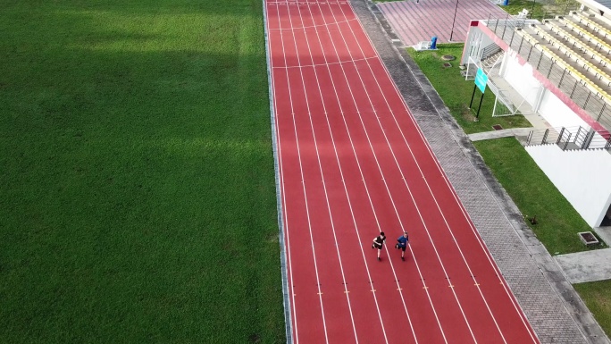 无人机视角下的运动亚裔中国父子早上在露天看台旁的田径场排队起跑，在跑道上奔跑，朝终点线跑去