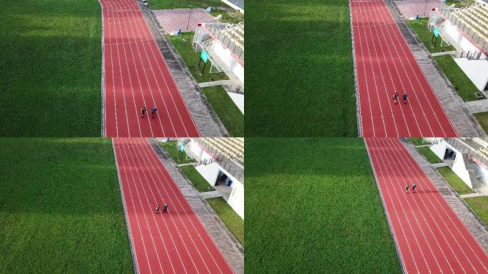 无人机视角下的运动亚裔中国父子早上在露天看台旁的田径场排队起跑，在跑道上奔跑，朝终点线跑去