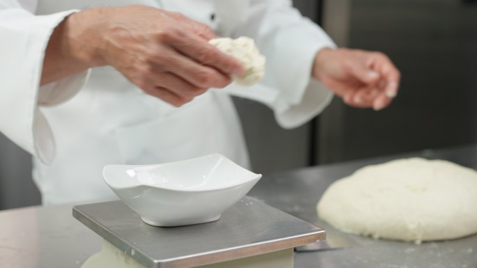 特写镜头：白色厨师揉捏和准备面团，在成型前分割和称重，在商业面包房厨房制作面包和馒头