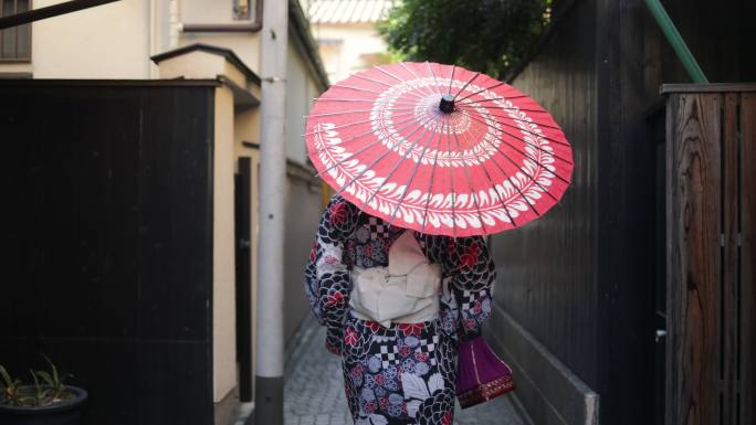 在Yukata的日本妇女在狭窄的小路上行走-使用纸伞