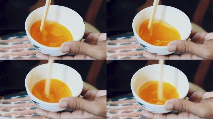 一个人在厨房的碗里搅拌鸡蛋的动作，用筷子将鸡蛋打匀。