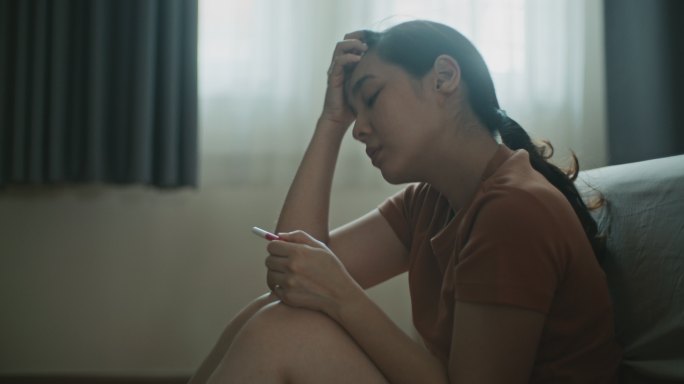 年轻的亚洲女性沮丧地看怀孕测试