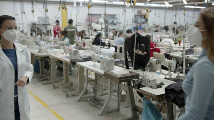 在一家工厂，拉丁美洲妇女戴着口罩，用肘互相问候