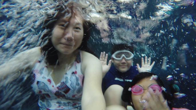 快乐的亚洲妈妈和孩子们在酒店的游泳池里玩得很开心，生活方式理念。