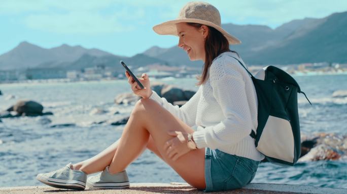 4k视频片段，一位快乐的年轻女子一边在海边放松一边用手机发短信