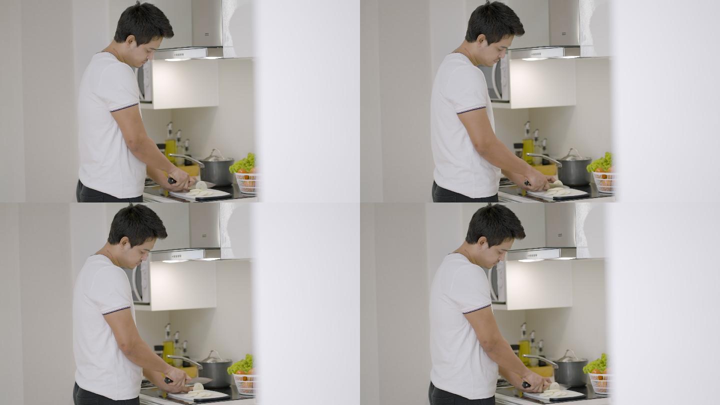 一名亚洲男子在厨房柜台上切洋葱，准备在家吃饭。