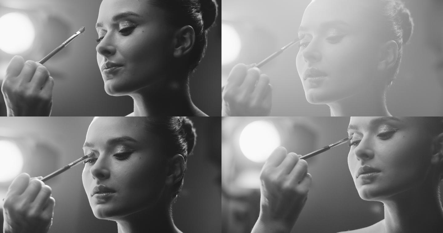 女孩脸的特写镜头。一位化妆师在片场上用化妆刷将阴影涂在女演员的眼睑上。黑白视频。