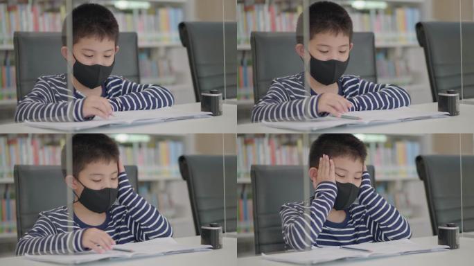 亚洲小男孩坐在图书馆做作业，茫然无聊，不想工作