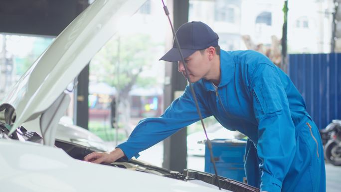 亚洲汽车修理工在修理厂工作时戴头盔。年轻的车辆服务经理男性工人打开汽车引擎盖，然后在车间进行检查和维