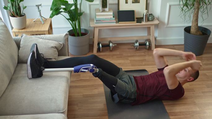 带假肢的年轻人在家里瑜伽垫上做仰卧起坐练习