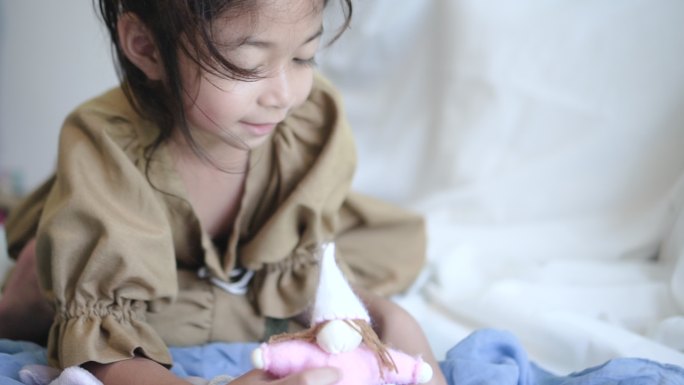 小女孩坐在沙发床上玩洋娃娃。