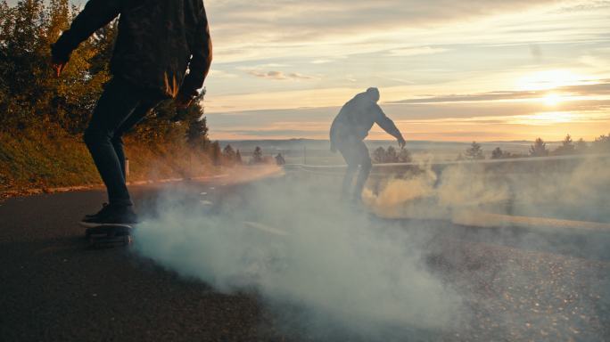 中景：年轻人在日落大道上玩着烟雾弹滑板
