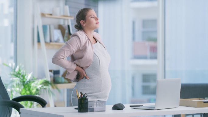 一名年轻孕妇在现代办公室使用笔记本电脑时背部疼痛的4k视频片段